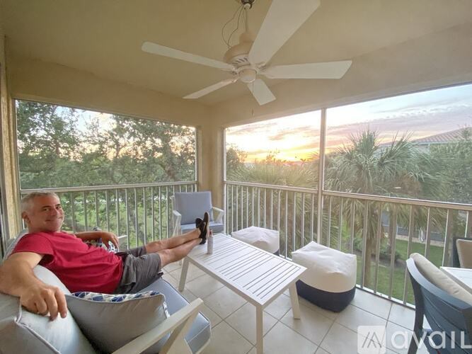 A man in a red shirt is sitting on a couch on a balcony with a ceiling fan.