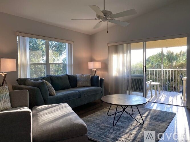 A living room with a grey couch, a round table, and a ceiling fan.