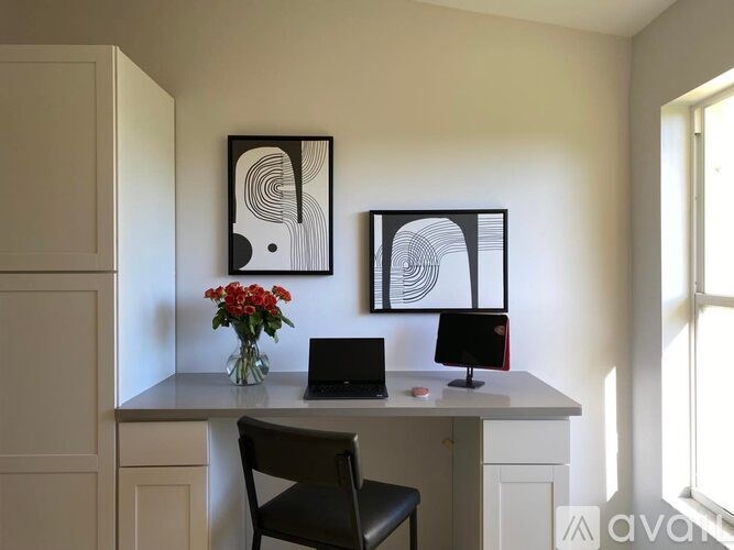 A desk with a laptop and a monitor with a black frame and a white frame with a black frame and a vase with red flowers on it.