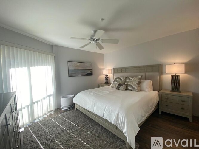 A bedroom with a large bed, a ceiling fan, and a painting on the wall.