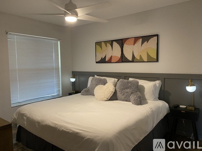 A bedroom with a white bed and a colorful abstract painting above it.