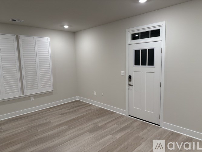A room with a white door and a window with white shutters.