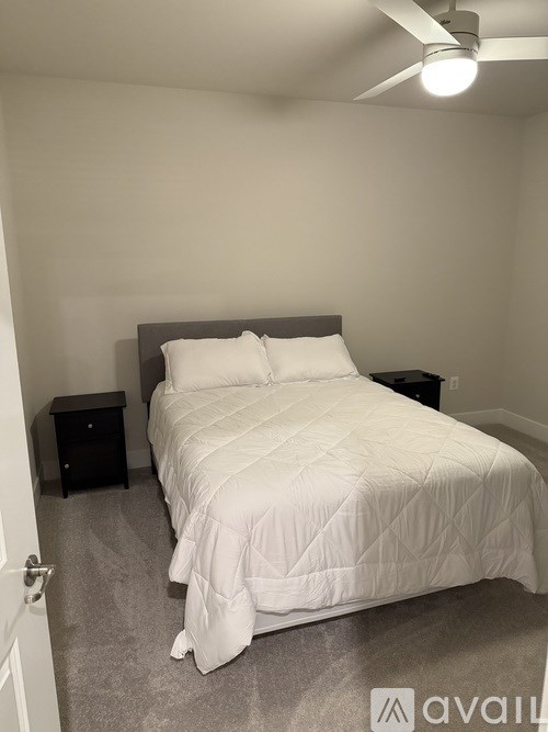 A bed with a white comforter and two pillows sits in a room with a ceiling fan.