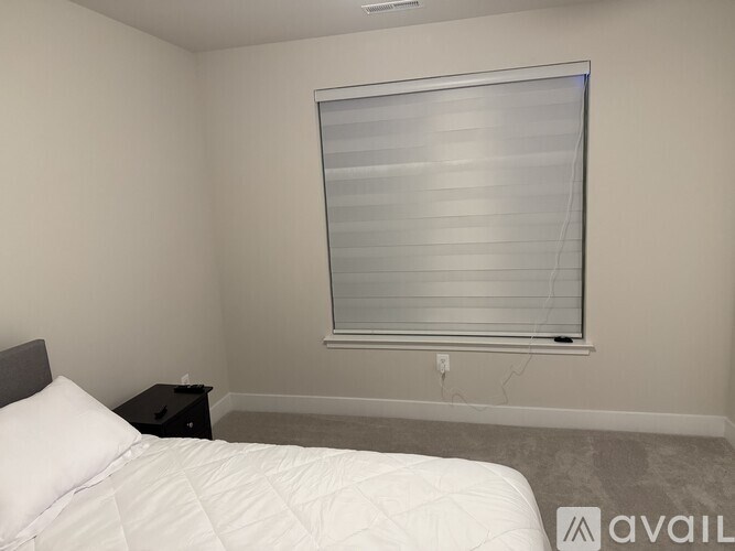 A bedroom with a bed, nightstand, and window with blinds.