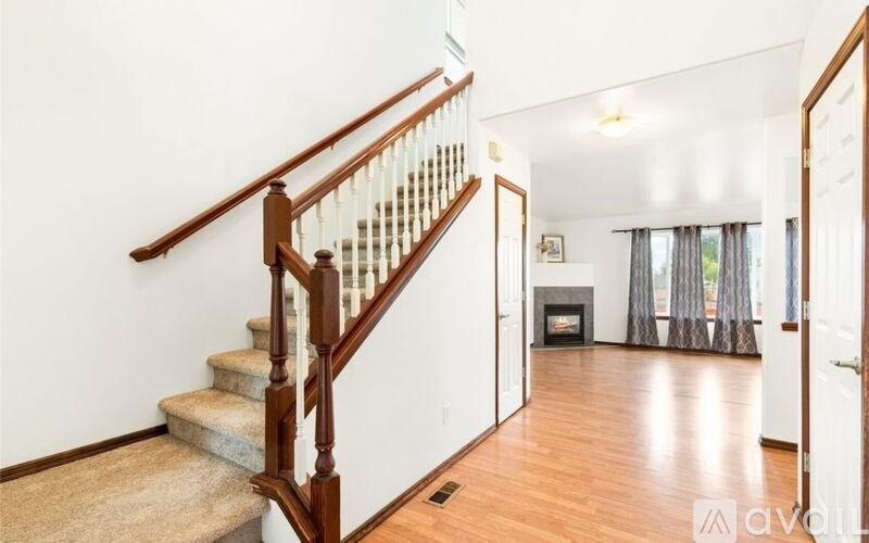 A wooden staircase with a beige carpeted landing leads to a living room with a fireplace.