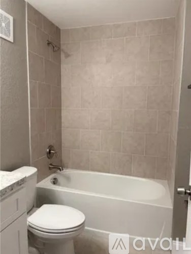 A white toilet sits next to a bathtub in a tiled bathroom.