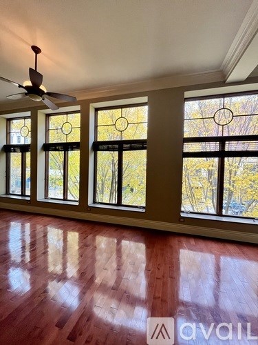 A room with a ceiling fan and large windows.