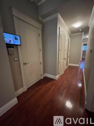 A hallway with a TV mounted on the wall and wooden floors.