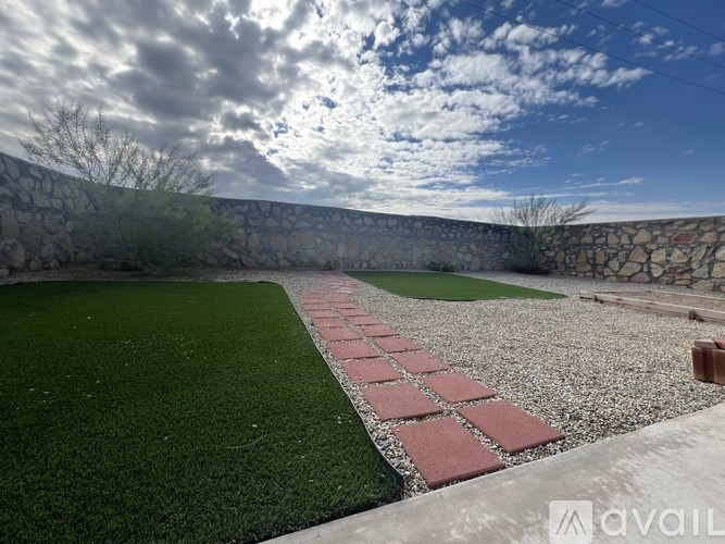 A stone wall with a grassy area in front and a brick pathway leading to a small building.