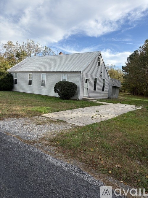 A white barn with a metal roof is situated in a grassy area with a road in front of it.