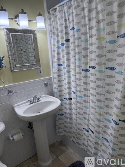 A white sink with a mirror above it and a shower curtain with fish on it.