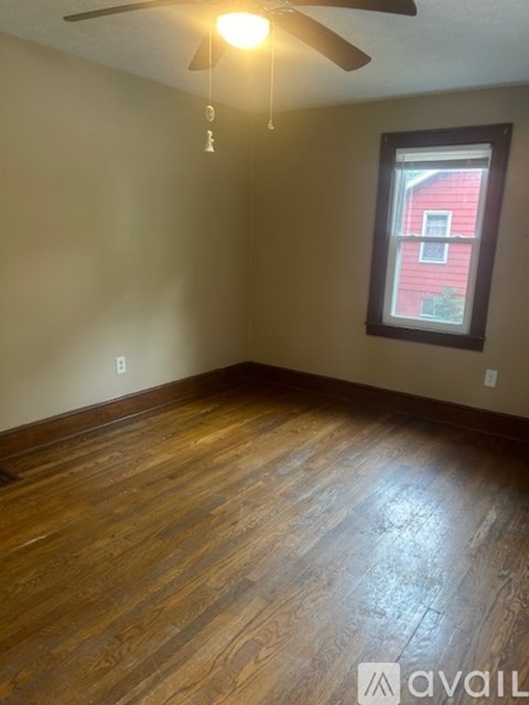 A room with a ceiling fan and a window showing a red house outside.