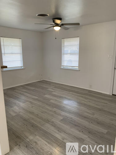 A room with a ceiling fan and light, two windows, and a wooden floor.