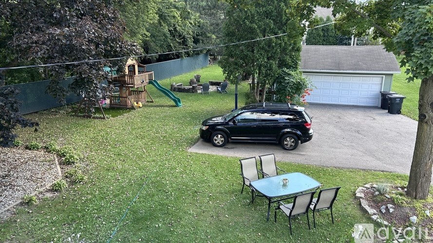 A black car is parked in a driveway next to a table and chairs.