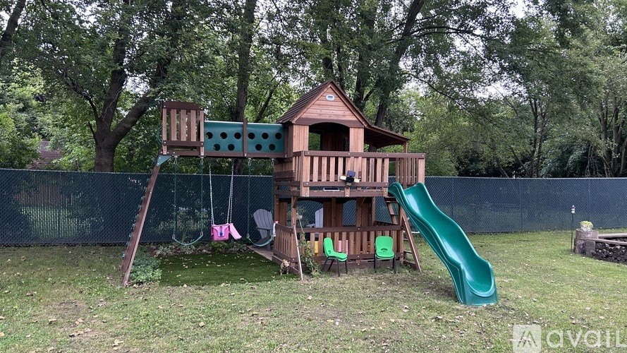 A wooden swing set with a green slide in a backyard.