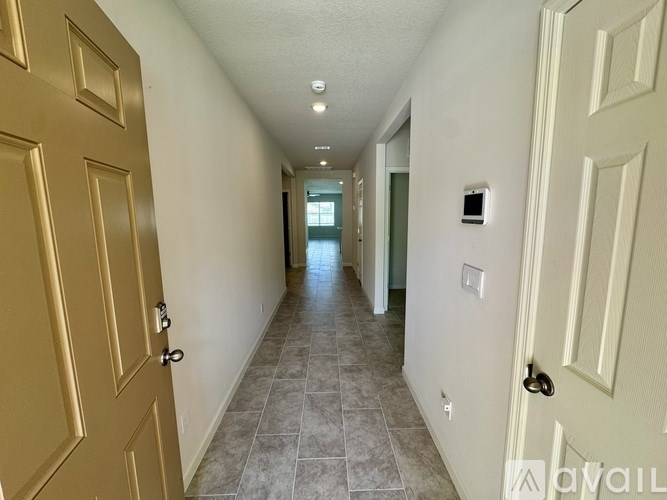 A hallway with tiled floors and white walls leading to a door.