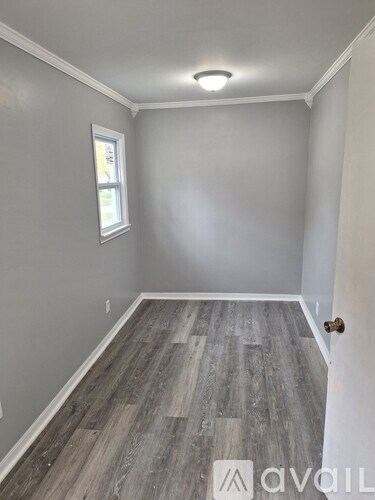 A room with grey walls and wooden flooring with a window.