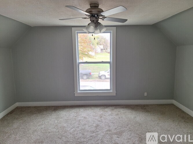 A room with a ceiling fan and a window overlooking a street.