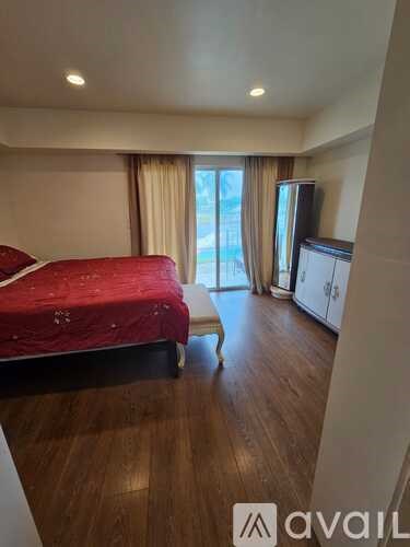 A bedroom with a red bedspread and wooden floors.