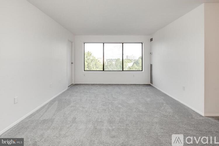 A large empty room with a carpeted floor and a window with a view of trees and buildings outside.