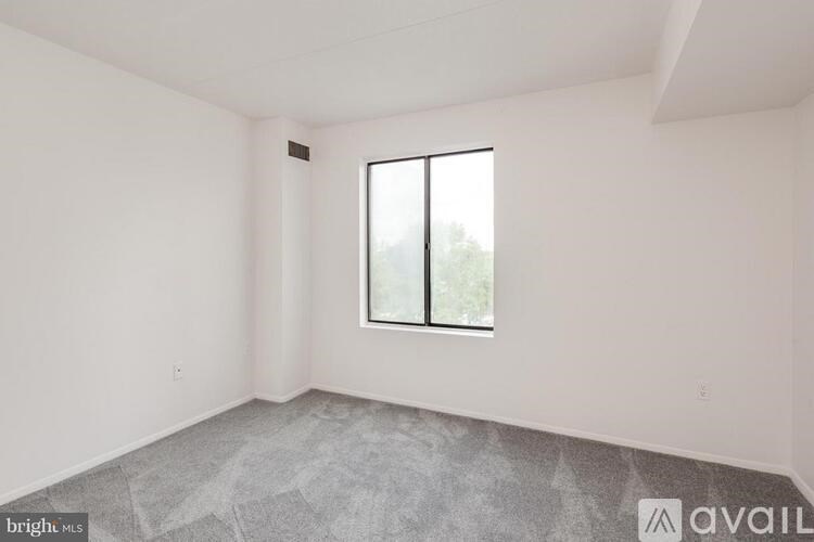 A spacious room with a large window and a grey carpet.