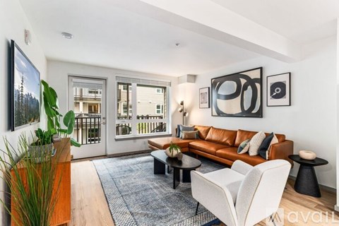 A living room with a brown leather couch, a white chair, and a painting on the wall.