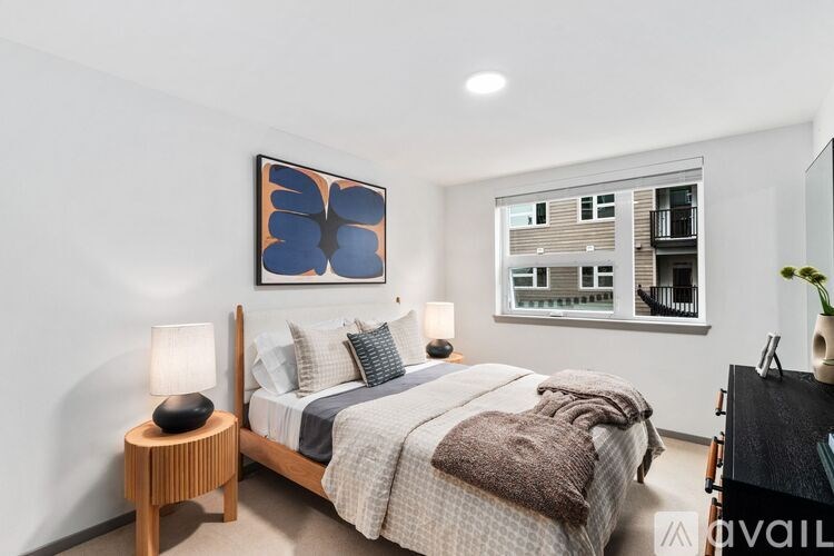 A bedroom with a bed, nightstand, and a window with a view of a building outside.