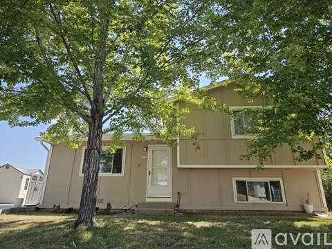 A beige house with a tree in front of it.