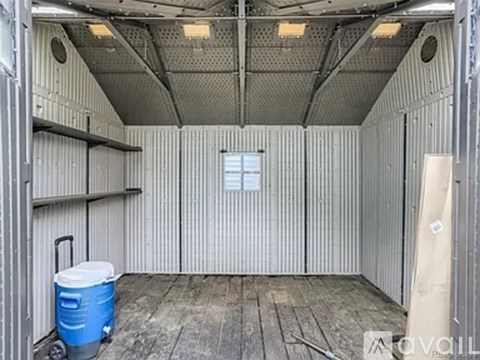 A blue cooler is on the floor of a metal shed.