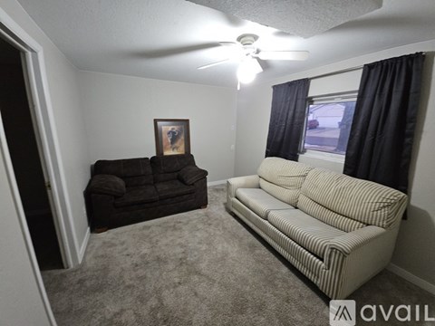 A living room with a black couch, a striped sofa, and a ceiling fan.