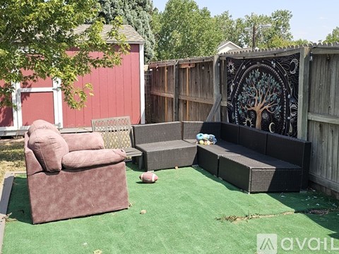 A backyard with a red shed, a brown couch, and a black tree mural on the fence.