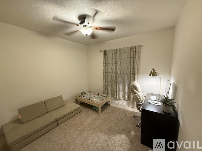 A living room with a couch, a coffee table, a desk, and a ceiling fan.
