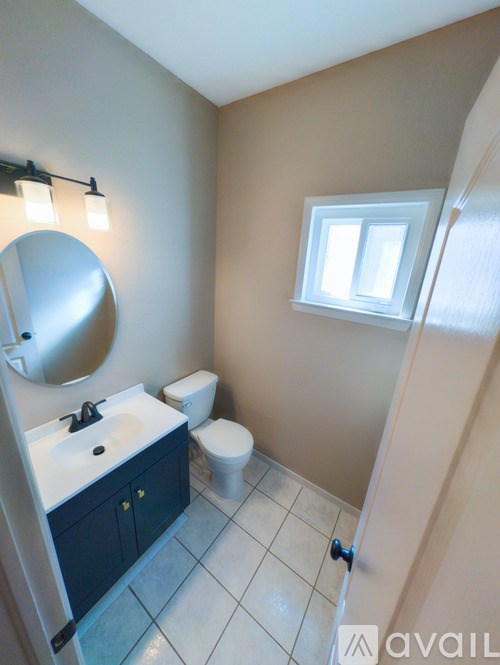 A bathroom with a sink, mirror, toilet and a window.