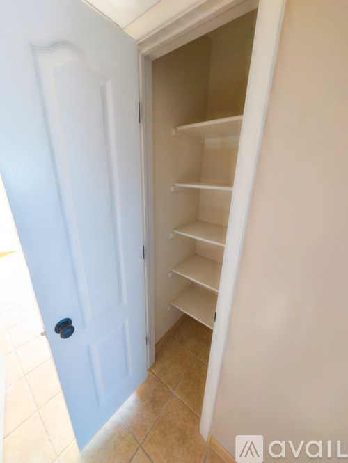 A white door with a black handle is open to a white hallway.