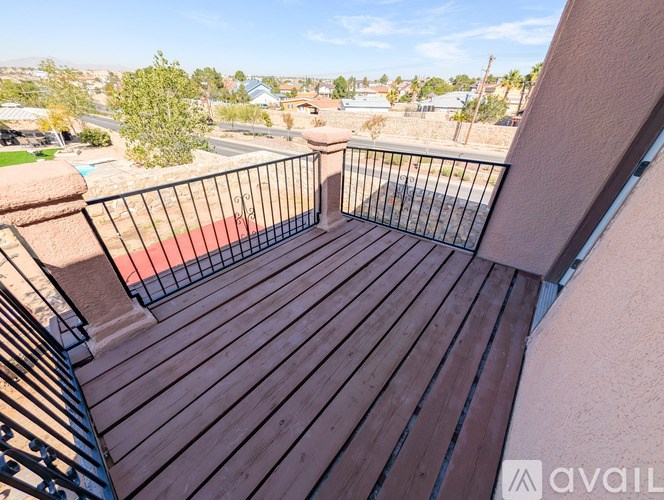 A balcony with a black railing and wooden flooring overlooks a residential area.