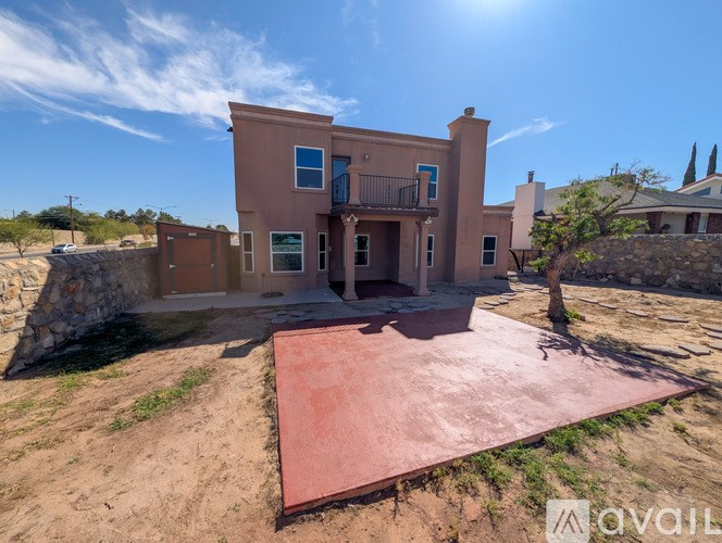 A house with a red roof and a balcony is surrounded by a dirt area.