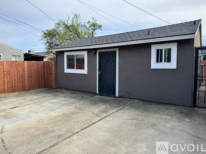 A gray house with a black door and a window is available for rent.