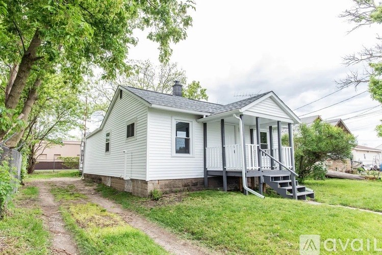 A small white house with a porch and a tree in front.