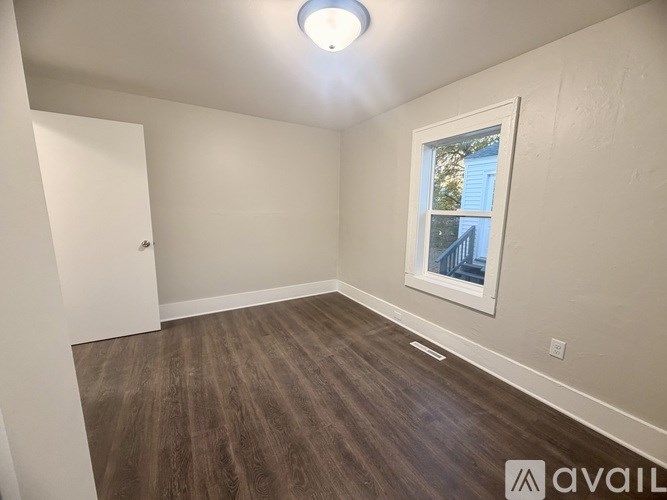 A room with a wooden floor and a window showing a blue house outside.
