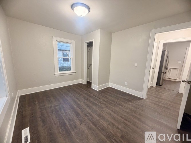 A room with wooden flooring and a window with a view of a building across the street.