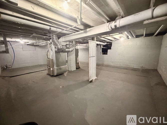 A spacious basement with a concrete floor and white walls, equipped with industrial-sized ductwork and pipes.