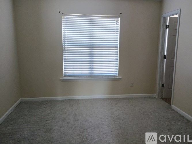 A room with a carpeted floor, a window with blinds, and a door.