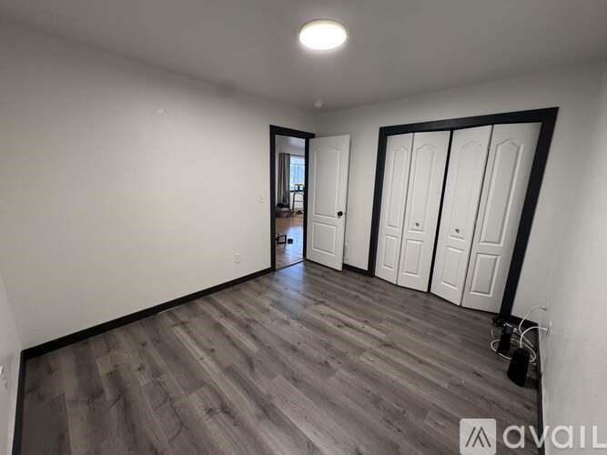 A room with wooden flooring and white walls, with a door on the left and three white doors on the right.
