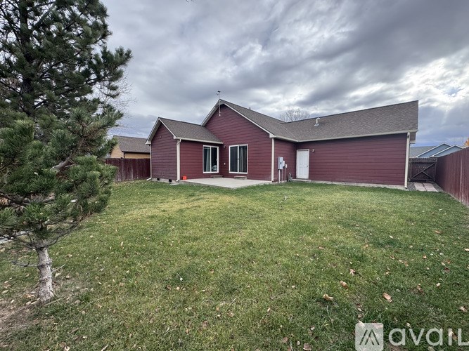 A red house with a white door and windows is surrounded by a grassy yard.