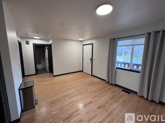A room with wooden flooring and a window with curtains.