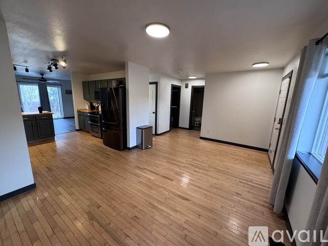 A spacious room with wooden flooring and a large window on the right side.