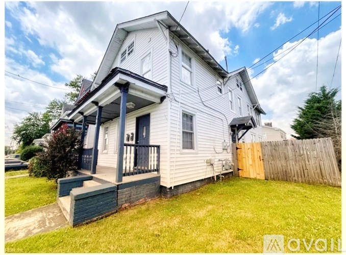 A two-story house with a porch and a fence in front.