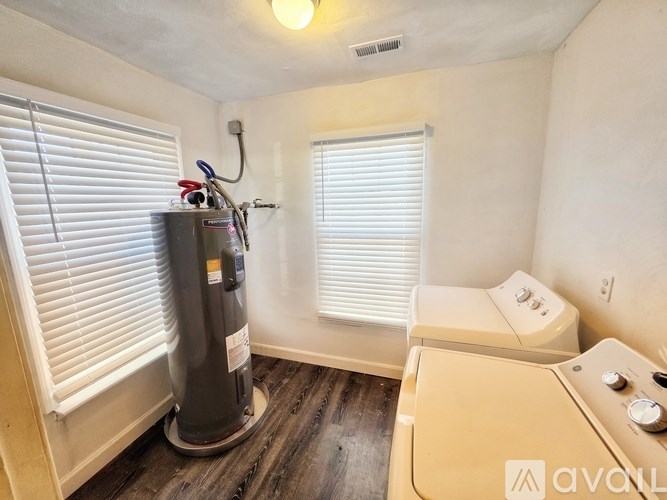 A room with a water heater and a window with blinds.