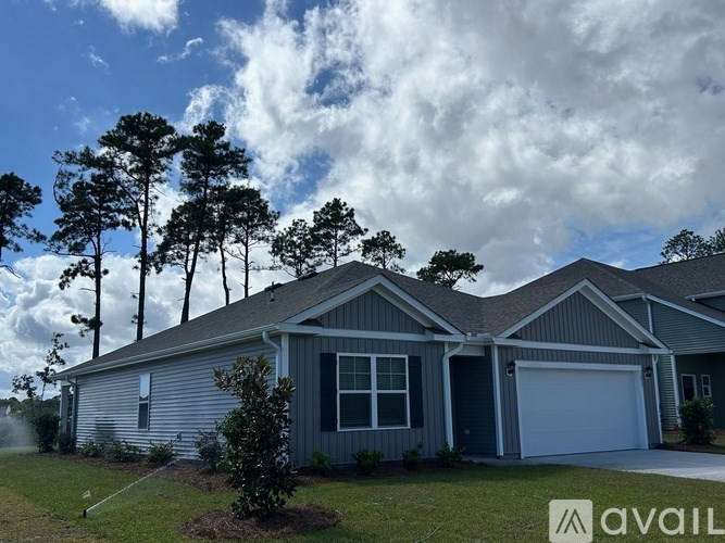 A house with a grey siding and a white garage door is surrounded by trees.
