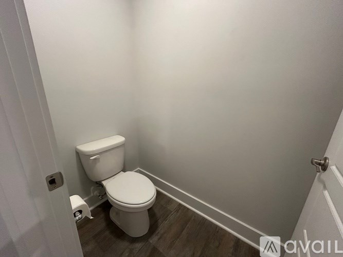 A white toilet in a small bathroom with wooden flooring.